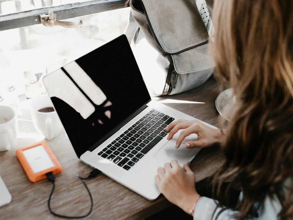 girl wearing grey long-sleeved shirt using MacBook Pro on brown wooden table